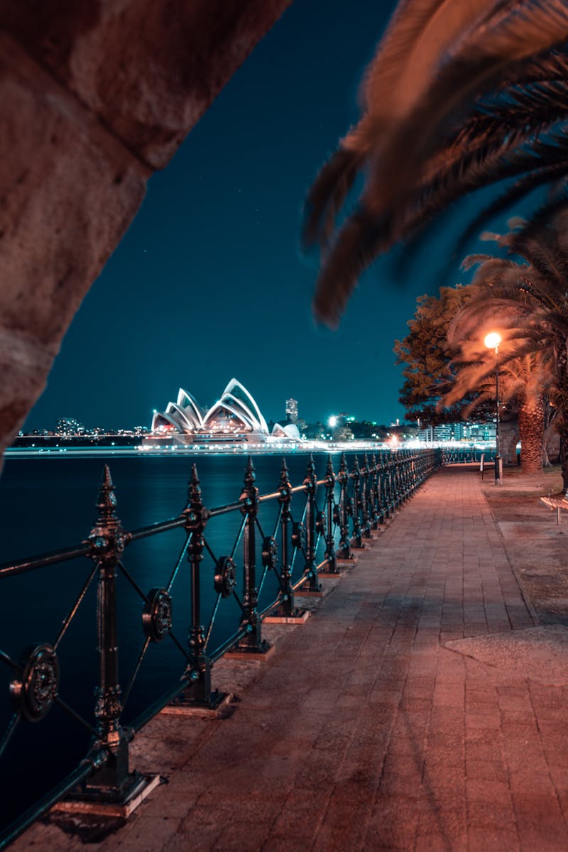 A serene night view of Sydney Opera House from a waterfront walkway, illuminated beautifully.